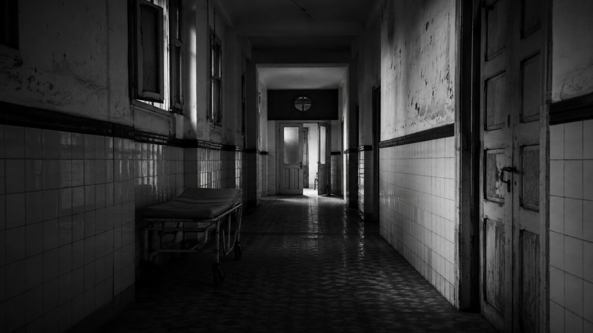 Pasillo antiguo de hospital mexicano con luz tenue, una puerta entreabierta al fondo y sombras largas sobre el piso, escena cinematográfica en blanco y negro sin texto.